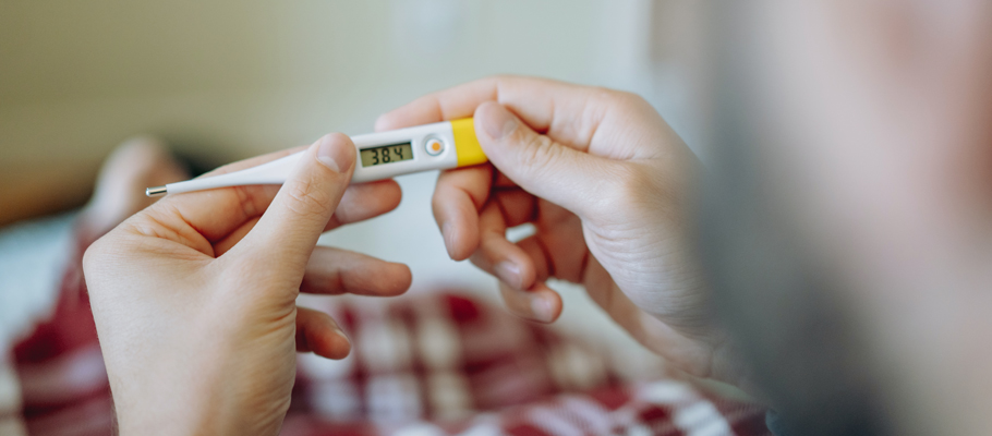 Persona sujetando un termómetro que indica fiebre