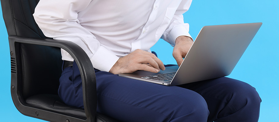 Hombre sentado en una silla con un ordenador y signos de incomodidad
